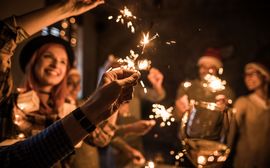 Several guests at a Christmas party hold up lit sparklers.