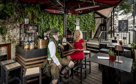 Ein Mann in bayrischer Tracht sitzt mit einer Dame in rotem Kleid an der Bar im Platzl Karree.