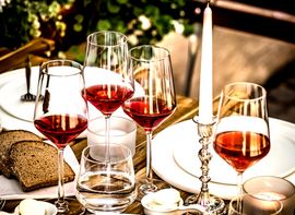 Detailaufnahme von vier Rotweingläsern, Tellern, Brot und einer Kerze aus einer Weinbar in München