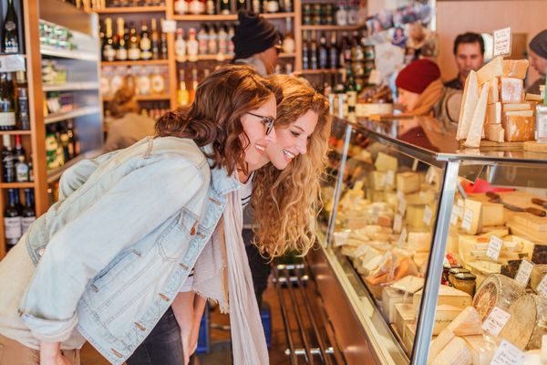 Viktualienmarkt Zwei junge Frauen betrachten die große Käseauswahl an einer Theke in der Schrannenhalle in der Münchner Altstadt.