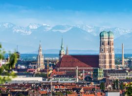 Blick über die Münchner Altstadt mit den Türmen der Frauenkirche vor den Alpen im Hintergrund.
