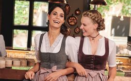 Two women with traditional Bavarian dresses on are laughing at the camera