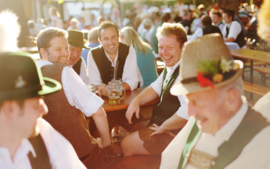 Visitors in traditional Bavarian attire are chatting in Ayinger Bräustüberl's beer garden.