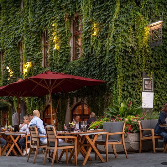 Outdoor area of the restaurant Pfistermühle where guests enjoy food and drinks under a garden umbrella.